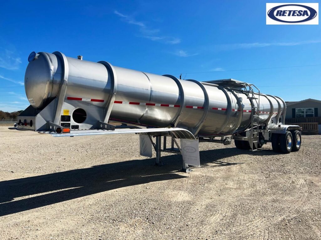 Tank trailer for transporting liquids, parked outdoors on gravel.
