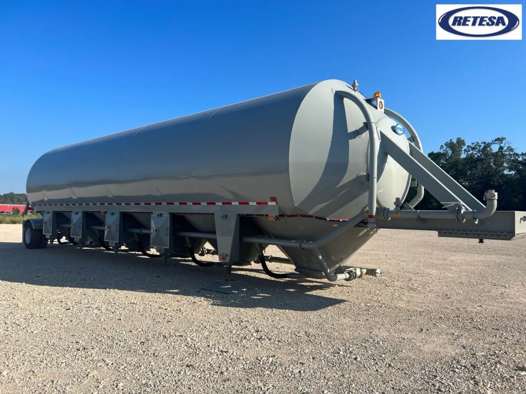 Large gray fuel tanker trailer parked outdoors on gravel surface under clear blue sky.